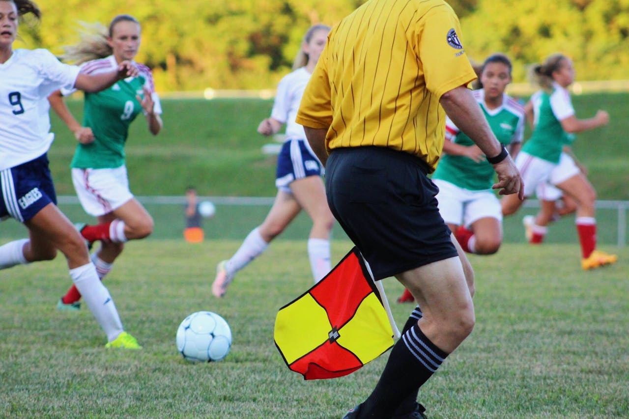 Womens soccer match featuring players and referee on field in motion.